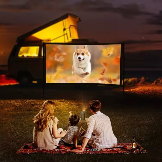 Petite famille regardant un film sous les étoiles lors d'un camping, utilisant un vidéoprojecteur portable pour une projection en extérieur.