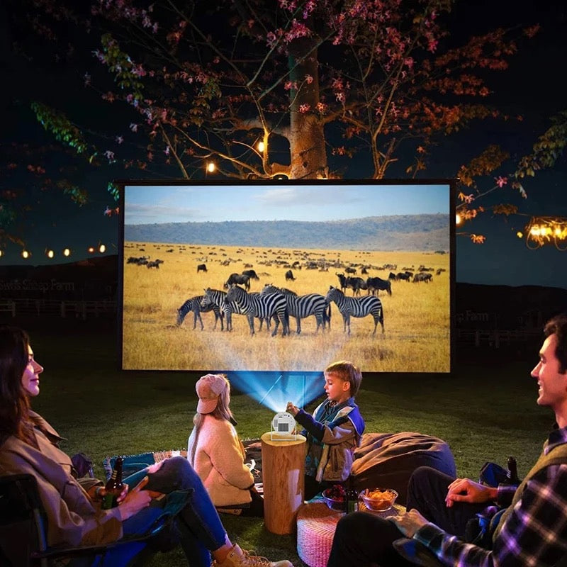 Famille réunie regardant un film en plein air la nuit avec un vidéoprojecteur portable 4K adapté à l’extérieur.